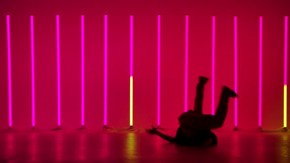 A Young Guy Performs Complex Acrobatic Figures in the Studio Against the Background of Multicolored