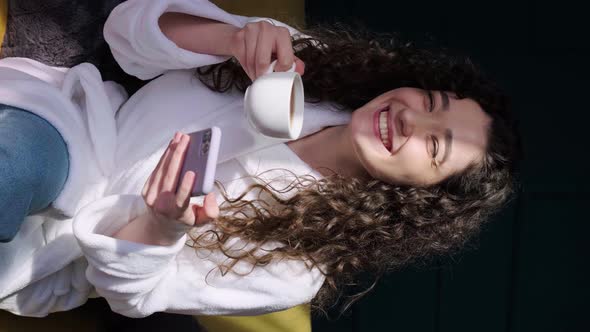 Curly Haired Girl Drinking a Tea at Home While is Writting on Phone After Having a Bath