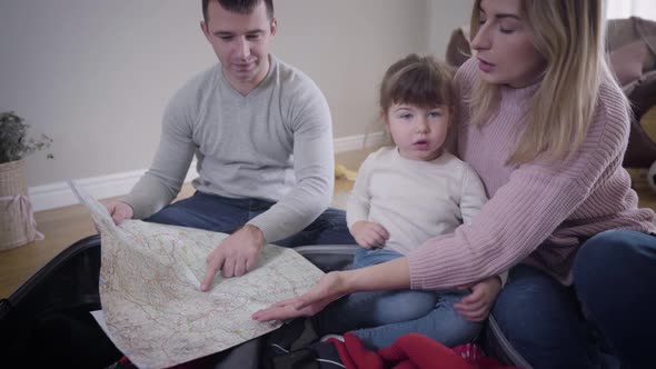 Portrait of Happy Young Caucasian Family Making Route for Future Trip. Smiling Young Man, Woman, and