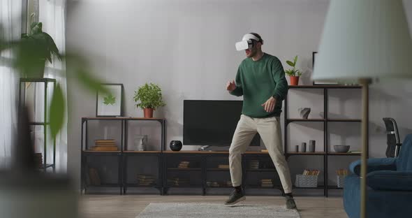 Young Man Is Using Virtual Reality for Entertainment Singing and Dancing in Room Having Fun Alone at