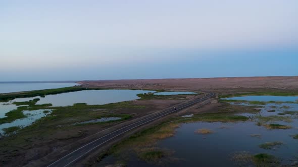 Aerial View of Car Driving on an Empty Road in the Desert Next To the Lake During Sunset