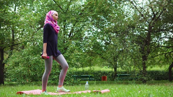 Young Muslim Woman in Burqa Crouching with Dumbbells in Summer Park