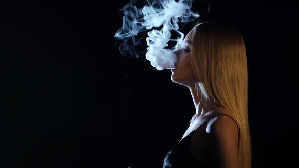 Girl of Extraordinary Beauty Smokes an Electronic Cigarette. Black Background. Side View