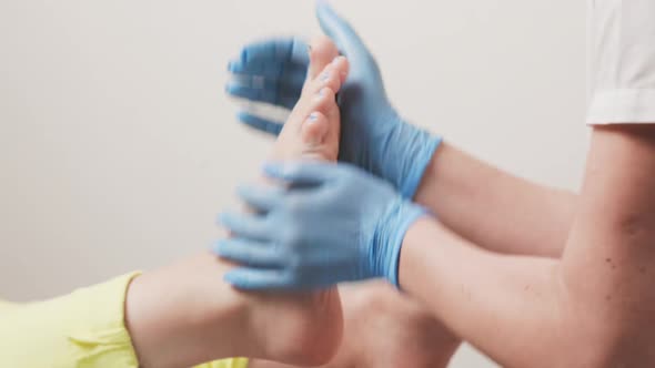 Master chiropodist in blue medical gloves massages a female foot. Closeup of hands and legs