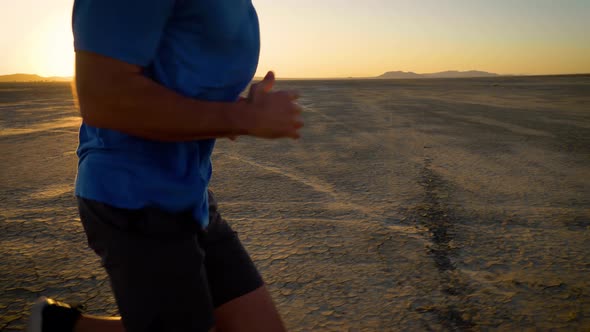 Athletic man working out with battle ropes on a dry lake at sunset