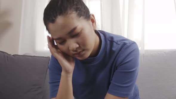 Asian woman wearing a blue shirt sitting on a sofa feeling very headache