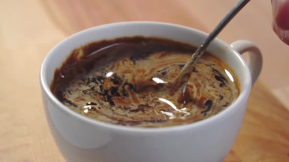 Stirring instant roasted coffee with a teaspoon in a white cup on a wooden table. Dissolving powder