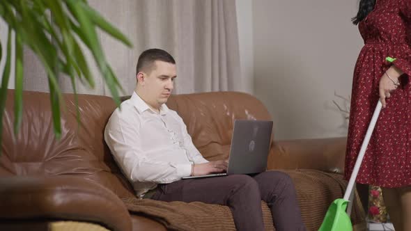 Brunette Caucasian Man Sitting on Couch Surfing Internet on Laptop Refusing To Help Pregnant Woman