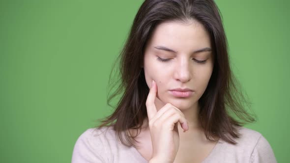 Young Beautiful Woman Thinking While Looking Down Against Green Background