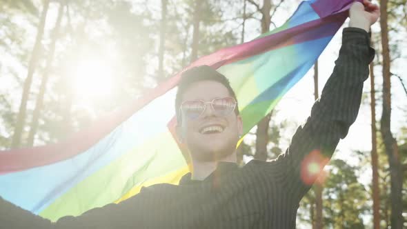 Homosexual Man Waving Rainbow Gay Flag on Sun Flare Light in Beautiful Summer Day. Happy Guy Wearing