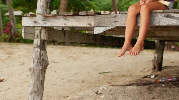 a Girl Waving Her Bare Feet While Sitting on a Wooden Bridge