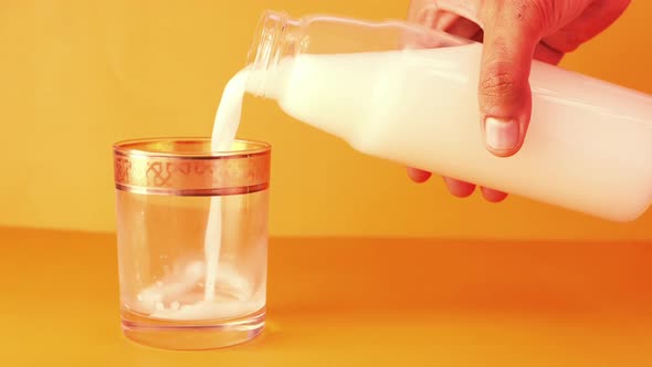 Pouring Milk Into the Glass on Orange Background 
