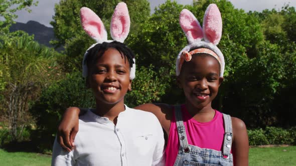 Smiling african american brother and sister wearing easter bunny ears embracing in garden