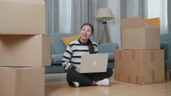 Asian Woman With Cardboard Boxes Comparing The House To Laptop After Moving Into A New House 