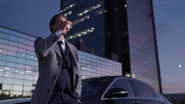 Portrait of a Cheerful Businessman Standing Near a Business Car and Drinking Coffee Top Manager in a