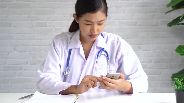 Young Asian Female Doctor Wearing a Surgeon Gown Using a Mobile Phone at the Office