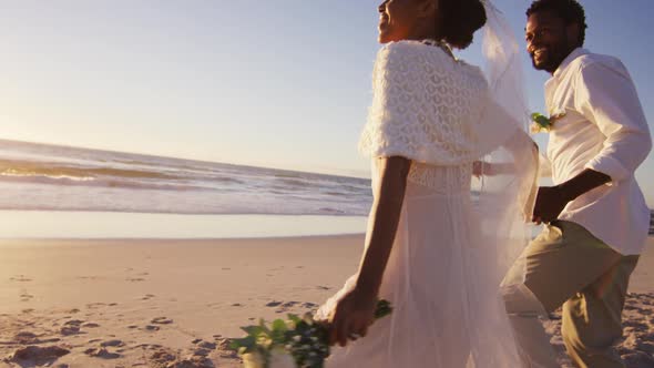 African american couple in love getting married, holding hands on the beach at sunset