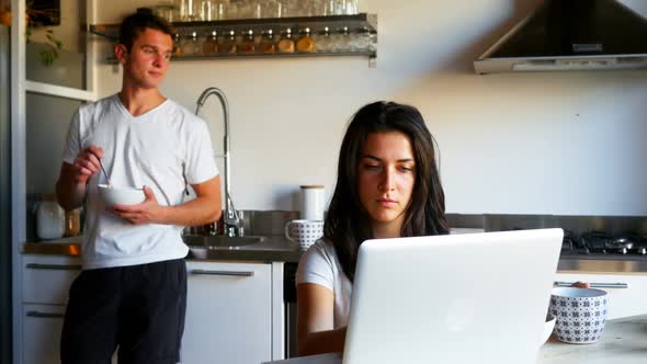 Woman using laptop while man drinking coffee in kitchen