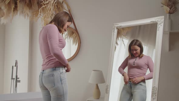 Unhappy Pretty Female Trying to Squeeze Into Old Tight Pair of Jeans in Front of Mirror