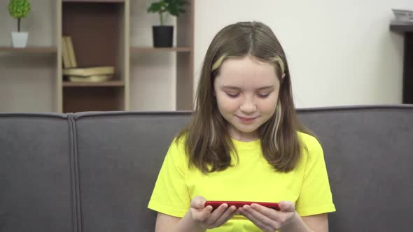 The Little Girl is Smiling and Looking at Her Phone While Sitting on the Couch