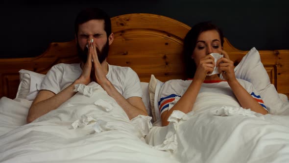 Couple covering nose while sneezing on bed