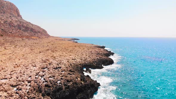 Drone shot flying over sea waves crashing against the rocky shore at Cavo Greko, Cyprus