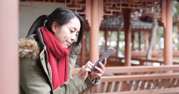Woman wearing winter jacket and use of mobile phone in china garden