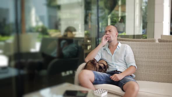 A Man Smokes While Sitting on a Chair on the Terrace of the Hotel