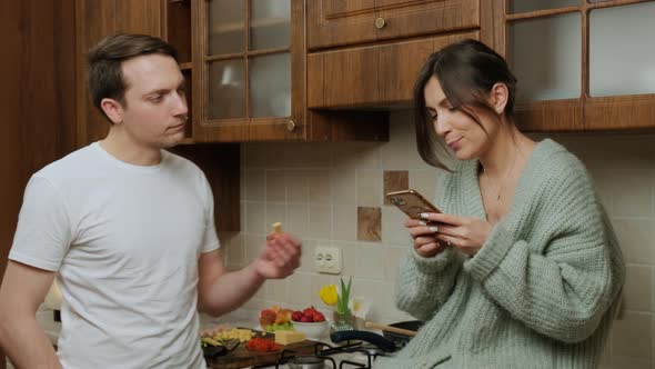 Young Man Prepares Food in the Kitchen While His Wife Is Surf the Internet