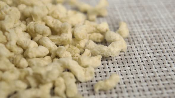Textured dry soy flakes fall into a pile on a plastic wicker mat