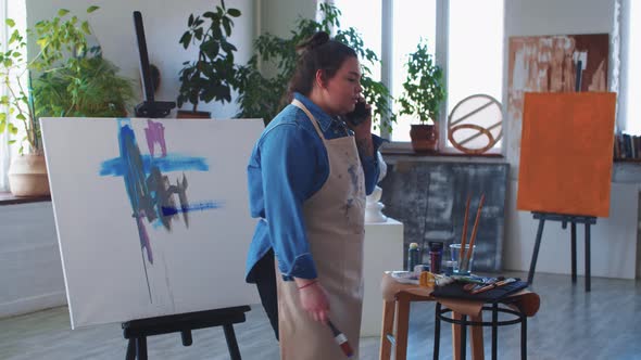 A Woman Paint Artist Talking on Her Phone in the Studio in the Middle of the Drawing Process