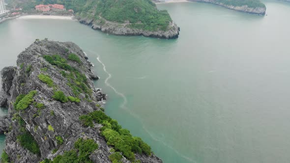 Aerial: flying over beautiful rocky coastline and promenade on the cliff at Cat Ba island, Vietnam