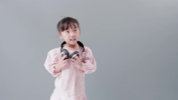 Cute Asian girl with headphones enjoy music and dancing, turning around happily in studio.