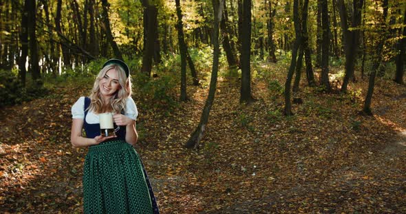 Happy Slavic Girl in National Costume Poses with a Mug of Beer in Autumn Forest