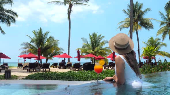 Travel Woman in Hat and Swimwear with Refreshment Drink Swimming in Pool