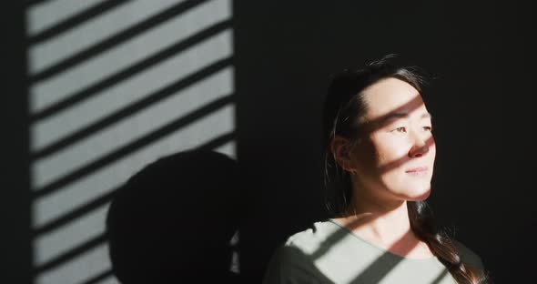 Thoughtful asian woman sitting on sofa close to window at home