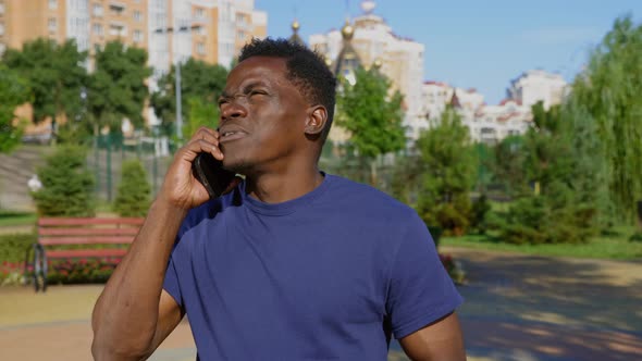 AfroAmerican Man Standing in Park Talking on Cell Phone and Looks Around