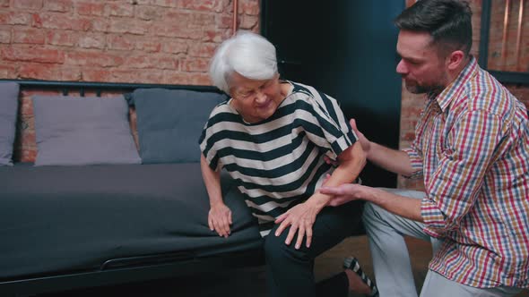 Caucasian Greyhaired Senior Woman Falling Down the Sofa Supported By Her Surprised Middleaged Son