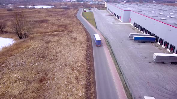 Buildings of logistics center, warehouses in the field near the highway, view from a height, trucks