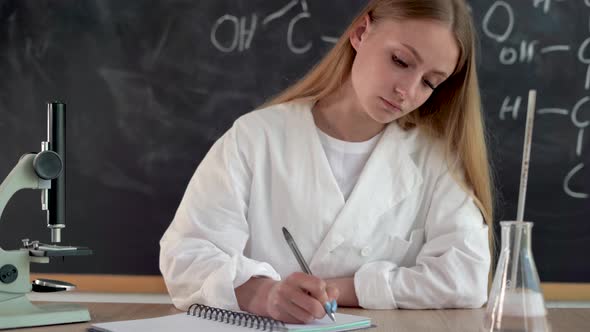 Tutor Chemistry Teacher at School Sits at a Desk Making Notes in a Notebook