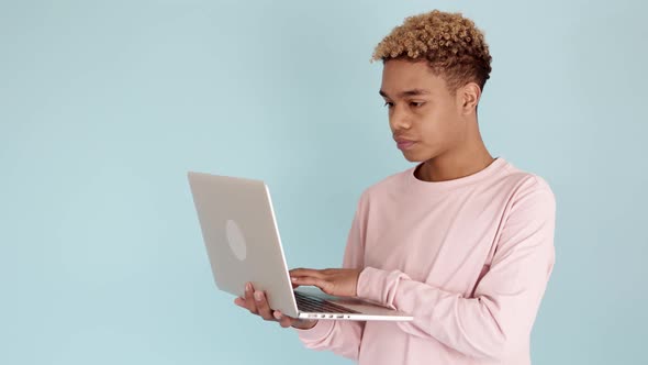 Young Worried Teenager Boy Reading Bad News on Laptop Against Blue Background