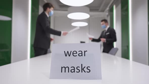 Wear Masks Message in Business Office with Blurred Caucasian Men in Coronavirus Face Masks Passing