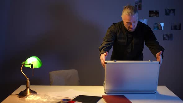 Police Officer Opening Briefcase Examining Evidence Standing in Dark Room with Table Lamp Light