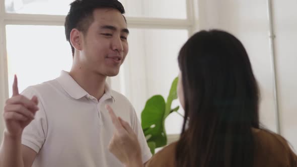 Happy young Asian couple dancing in the living room listening to music at home.