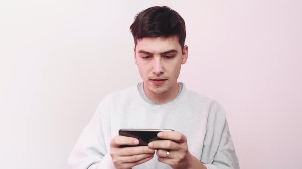 A Man Playing Mobile Games on His Phone Against a Light Background