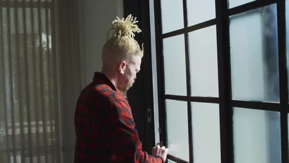 Thoughtful albino african american man with dreadlocks looking at the window