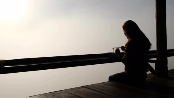 A woman eating noodle while sitting on wooden balcony with beautiful sunrise on foggy day