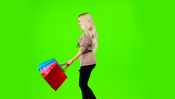 Blonde Girl Carries a Lot of Different Color Packages. Green Screen. Side View