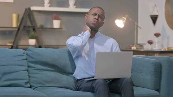 African Man with Laptop Having Neck Pain on Sofa