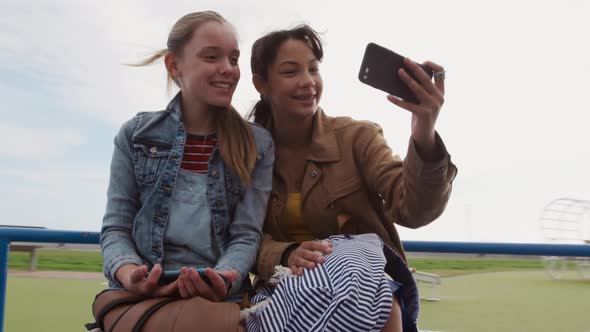 Front view of a Caucasian and a mixed race girl taking selfie on a merry-go-round